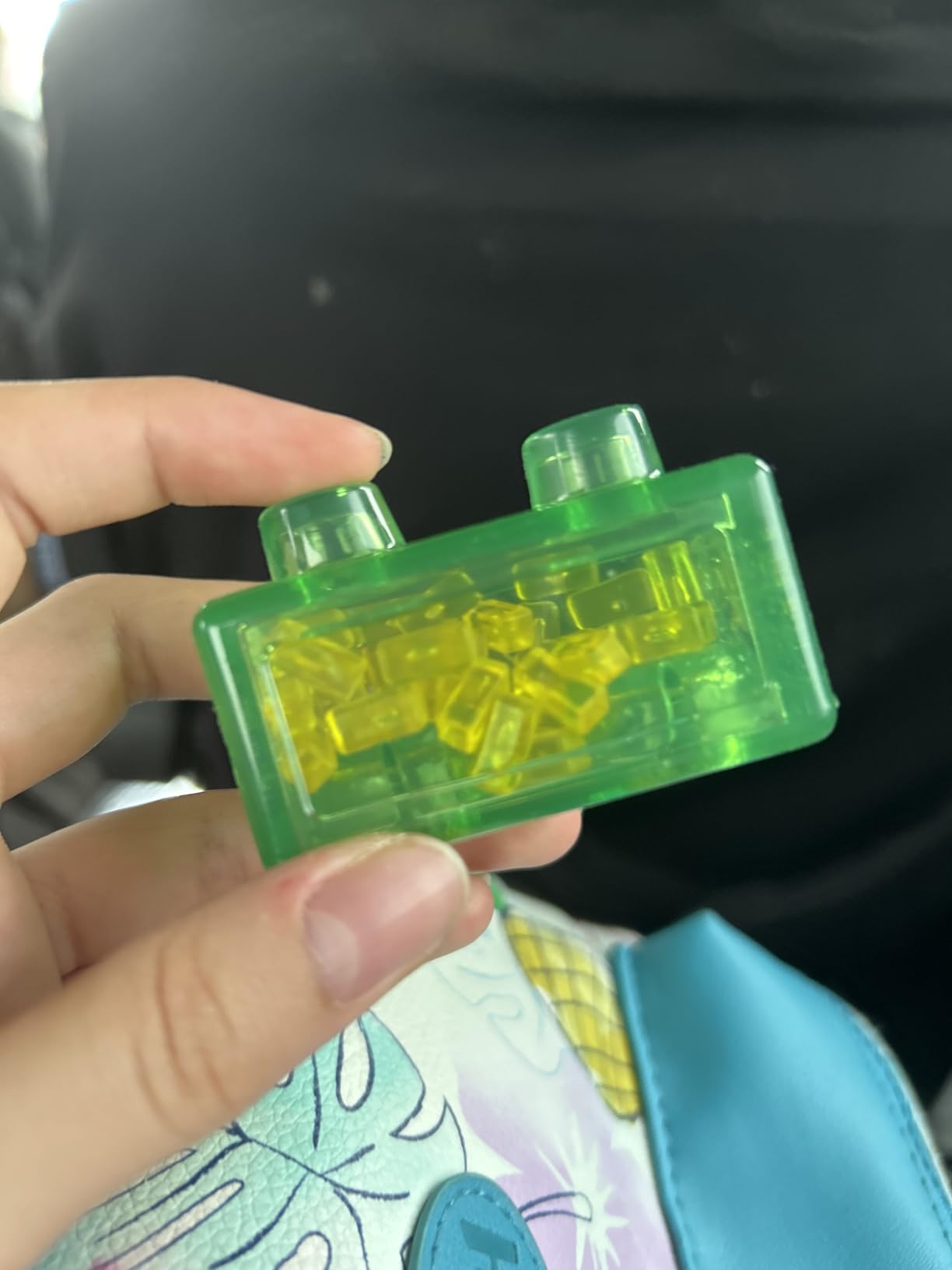 Green Jelly Blox block held between two fingers, yellow mini bricks visible inside the clear shell