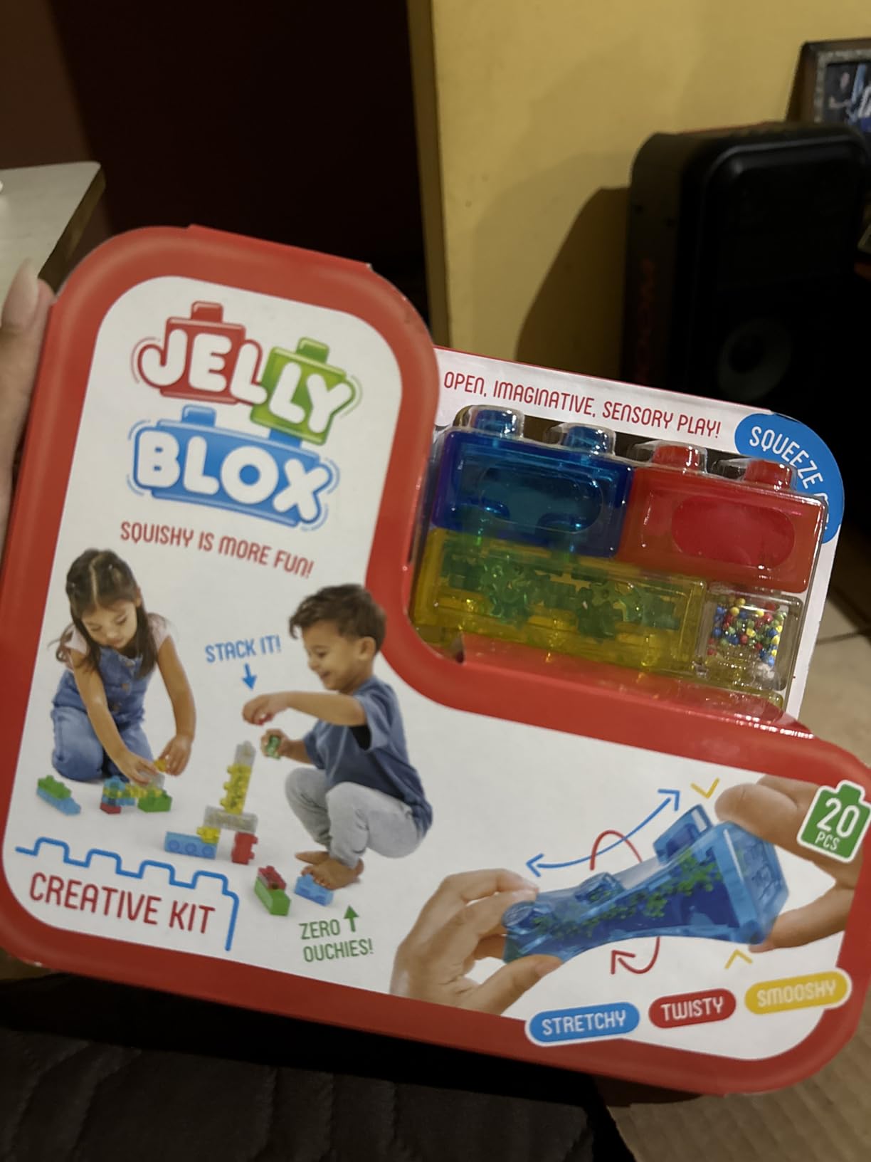 Jelly Blox Creative Kit box held up in a living room, blue, red and yellow blocks showing through the window