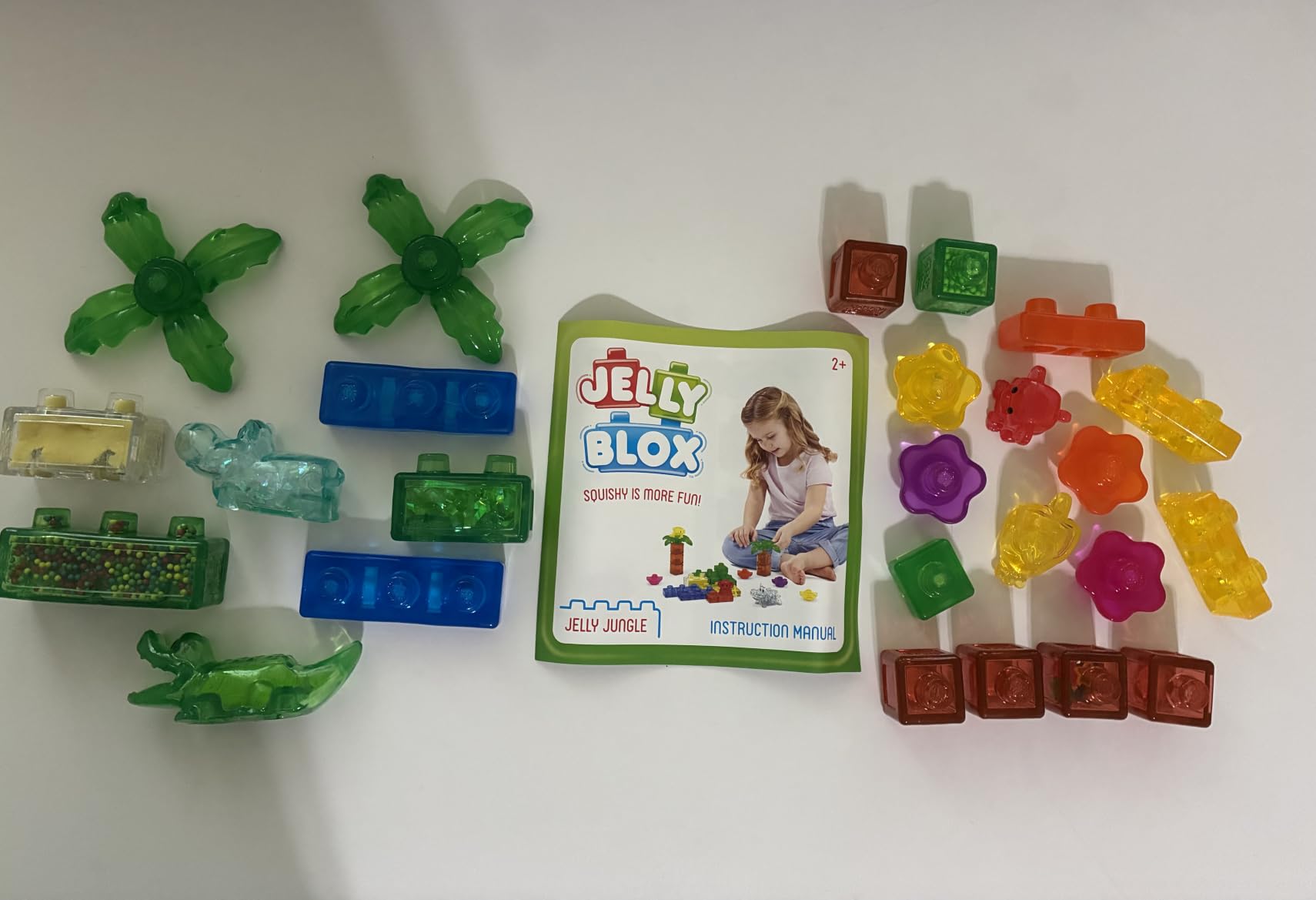 Jelly Jungle pieces spread on a white table around the instruction sheet: palm trees, crocodile, hippo and flower blocks